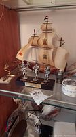Wooden model ship with sails and three metal figurines on a stand