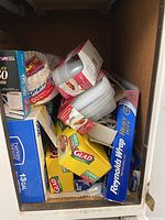 Kitchen cabinet shelf containing various kitchen disposable items: aluminum foil, sandwich bags, garbage bags, and Rubbermaid Take Alongs containers.