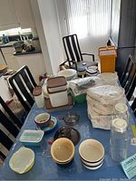 Wide view on dining table showing assorted Pyrex, Corningware and Tupperware containers, bowls, and pitchers.