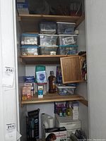 Full view of open linen closet with wooden shelves filled with labeled plastic bins, household items, appliances, first aid and batteries.