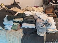 Photo of assorted bath towels, washcloths, sheets, and pillowcases piled and folded on a bed in multiple neutral and colored tones.