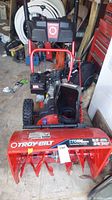 Front view of red Troy-Bilt snow blower showing auger housing, engine, handlebars and wheels