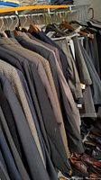 Photo of men's suit jackets in various colors and patterns hanging on a rack with shoes below.