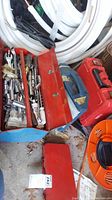 Metal toolbox open showing various sockets, wrenches, screwdrivers, and other hand tools along with a Rubbermaid container and the Milwaukee red case nearby
