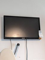 Front view of Samsung television mounted on wall, showing screen, bezel, and control buttons on lower right bezel.