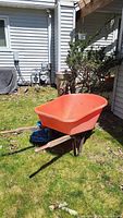 Full view of the plastic wheelbarrow with wooden and metal base sitting on grass outdoors.