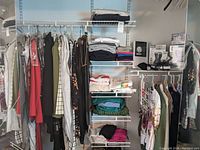 Wide shot showing multiple racks holding assorted women's clothing such as pants, jackets, dresses, and folded tops on shelves.