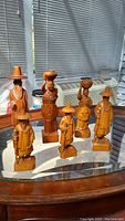 Seven carved wooden human figurines displayed on a glass surface showing variety in attire and posture, some with hats and baskets.
