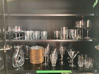 Shelf with assorted glass barware including wine glasses, tumblers, decanter, martini glasses, and a leopard print ice bucket.
