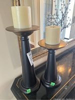 Photo of two metal candle holders with ivory pillar candles, showing overall height difference and design details.