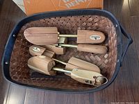 Top view of two sets of adjustable cedar shoe trees placed inside a dark woven basket with handles.