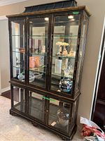 Front view of two-piece black wooden pagoda style glass display cabinet with hand-painted Asian motifs, glass doors and shelves, upper and lower sections, and interior lighting.