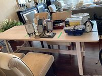 Dining table and bench with various household items on top, showing the light wood finish and construction details.