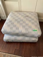 Two stacked square floor pillows with a checkered light pattern under ambient indoor lighting on wooden floor.