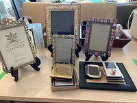 Full view of seven picture frames of varying sizes and styles arranged on a table with three black display stands and additional small items.