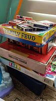 Stack of boxed board games and playing cards including Family Feud and The Game of Life