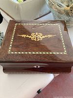 Closed view of wooden humidor showing decorative golden inlay on lid and front, keyhole in front center.