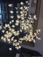 Full view of the illuminated white flower light tree showing the entire arrangement and metal base on a dark surface.