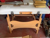 Front view of the folding massage table showing wooden legs, metal latches, carrying handles, and vinyl padded surface.