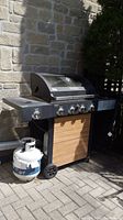 Full view of Master Forge black gas barbecue grill with wood accent front and one propane tank at the side.
