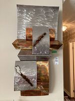 Front view of the metal sculpture showing the layered metal plates with a brushed silver and rusted copper finish.