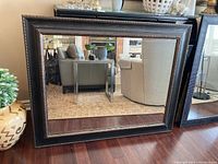 Mirror showing reflection of living room area, placed on floor against wall, highlighting frame details and bevelled glass edge