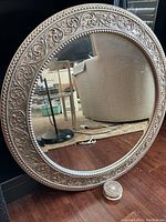 Front angled view of the round mirror showing the decorative frame and hanging chain.