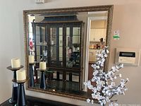 Full front view showing the entire mirror, reflecting a cabinet and candles.