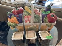Front view of three ceramic baskets with fresh vegetables on top and silver textured square bases as candle holders