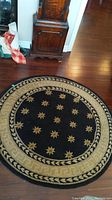 Full view of the round black rug with gold star patterns and Greek key style border, placed on wooden floor near furniture.