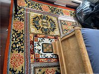 Full view of the wool rug on floor alongside wooden furniture showing floral and geometric patterns.