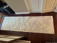 Full view of the rectangular wool runner rug laid on dark wood floor, showing the entire length and embossed floral pattern design.