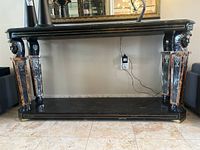 Front view of the rectangular black stone side table showing four legs with Egyptian style carved faces and metal inlay accents on edges.