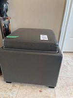 Side view of dark gray faux leather square stool with visible wear and scratches. Shows the removable cushioned top that functions as a tray on storage compartment.