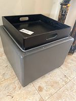 Gray upholstered square stool ottoman with a removable black wooden tray placed on top, showing condition and materials.