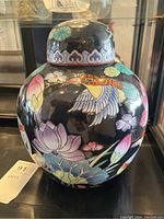 Full view of the urn with lid showing floral and bird painted decorations on black ceramic.