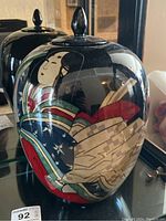 Front side view of the black ceramic urn showing a painted geisha in colorful kimono.