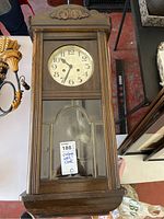Front view of vintage wooden wall clock with glass front and carved detail on top.