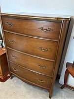 Full front view of medium wood 4-drawer dresser with brass-colored pulls, showing curved drawer fronts and overall structure.