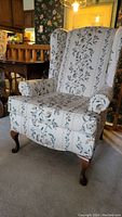 Front view of wingback chair with floral upholstery and wooden cabriole legs, small rolled arms.