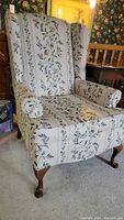 Front angled view of wingback chair showing floral upholstery and wooden legs.