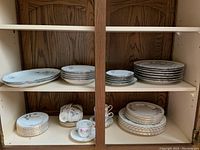 Two shelves of china including multiple plates, cups and saucers organized by type.
