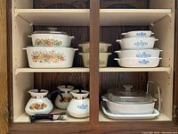 Shelf with Corning Ware casseroles and coffee pots in Cornflower and Spice of Life patterns, stacked and displayed.