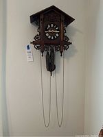 Full view of the wooden cuckoo clock hanging on a wall showing carved leaf details and pine cone weights hanging from chains.
