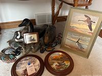 Overview of 12 painted wooden ducks, 1 wooden goose, 2 framed collector plates with duck scenes, a framed goose print, and a small wooden framed art piece with geese image on carpeted floor.