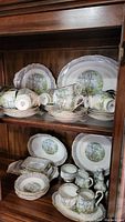 Multiple pieces including oval platters, serving plates, teacups, saucers, creamers, sugar bowls, salt and pepper shakers on wooden shelf
