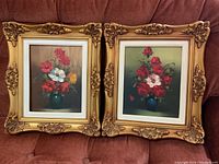 Photo of both framed floral paintings side by side showing ornate gold frames and colorful floral bouquets.