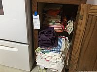 Cabinet with stacks of folded kitchen linens including tablecloths and tea towels.