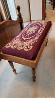 Full view of padded needlepoint seat bench with oak frame and turned legs on carpeted floor.