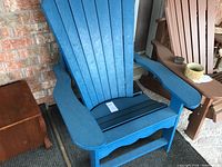 Front view of blue recycled plastic Adirondack chair against brick wall next to brown Adirondack chair and small wooden side table